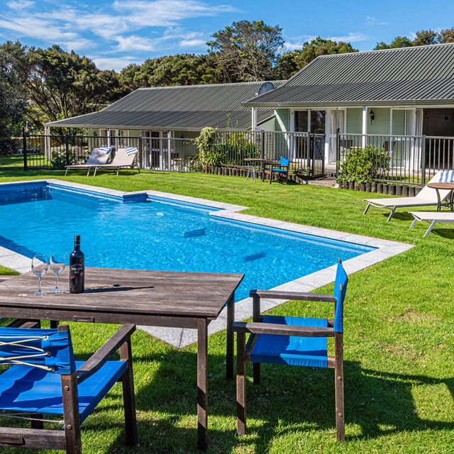 Outdoor swimming pool with table and chairs set on a grassy area at Ash Grove Motel, surrounded by guest rooms on a sunny day