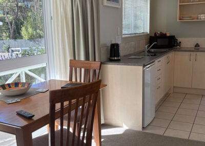 Kitchenette and dining area in the Deluxe King Studio at Ash Grove Motel, with large windows overlooking the garden.