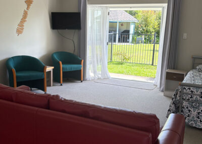 Spacious living area in the One Bedroom Unit at Ash Grove Motel with seating, TV and garden access.