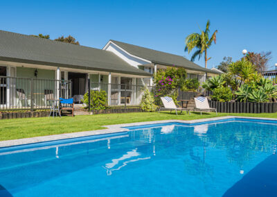 Outdoor pool area at Ash Grove Motel in Paihia, with sun loungers, gardens, and studio units overlooking the pool.