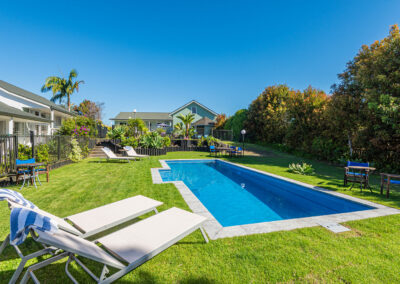 Swimming pool at Ash Grove Motel in Paihia, surrounded by sun loungers, garden seating, and landscaped greenery under a clear blue sky