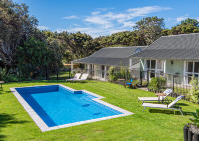 Outdoor swimming pool at Ash Grove Motel in Paihia, with sun loungers, garden seating, and studio units overlooking the pool.