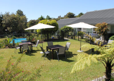 Outdoor seating area with umbrellas and garden views at Ash Grove Motel in Paihia, with the swimming pool and studio units nearby.