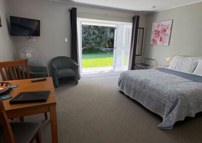 Interior of a Queen Studio Unit at Ash Grove Motel in Paihia, featuring a comfortable bed, dining area, seating, and sliding doors opening to the garden.
